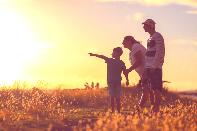 man and woman holding hands while walking on grass field during sunset